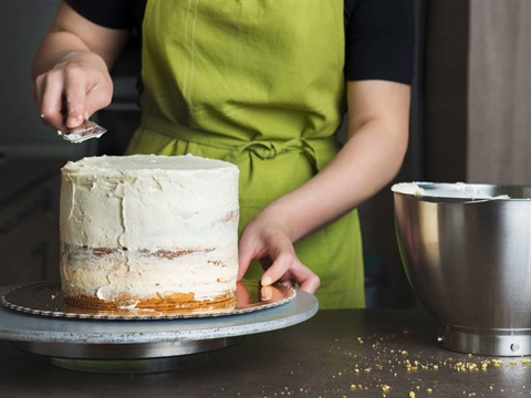 A person wearing an apron glazing a cake with a spatula